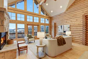 Living area with a stone fireplace, log walls, wood-type flooring, high vaulted ceiling, and a mountain view