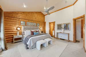 Carpeted bedroom featuring rustic walls, a ceiling fan, and high vaulted ceiling