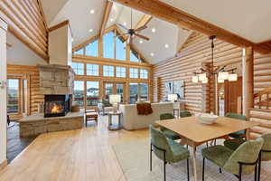 Dining space featuring high vaulted ceiling, rustic walls, hardwood / wood-style flooring, beam ceiling, and a fireplace