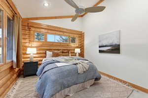 Bedroom with rustic walls, vaulted ceiling, and ceiling fan