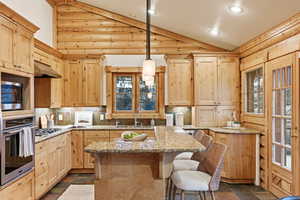 Kitchen with light brown cabinets, lofted ceiling, appliances with stainless steel finishes, stone tile flooring, and a breakfast bar