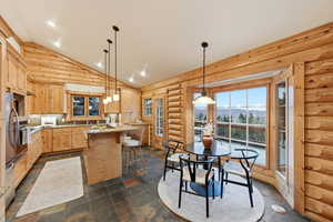 Kitchen with light brown cabinets, pendant lighting, a kitchen breakfast bar, log walls, and a center island