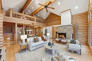 Living room featuring rustic walls, high vaulted ceiling, a stone fireplace, wood-type flooring, and beam ceiling