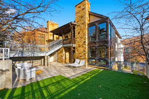 Rear view of house featuring a chimney, a patio, a balcony, and stone siding