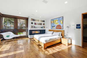 Bedroom with a glass covered fireplace, light wood-style flooring, and recessed lighting