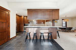 Kitchen featuring a kitchen bar, brown cabinetry, a peninsula, light countertops, and recessed lighting