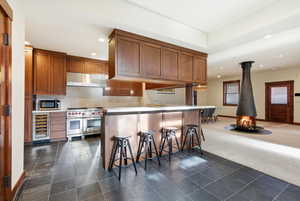 Kitchen with a breakfast bar area, recessed lighting, dark carpet, a wood stove, and beverage cooler