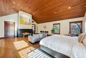 Bedroom featuring hardwood / wood-style flooring, a warm lit fireplace, a vaulted wood ceiling, and recessed lighting