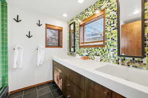Bathroom featuring double vanity, backsplash, healthy amount of natural light, recessed lighting, and dark tile patterned floors
