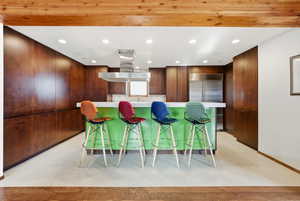 Kitchen featuring modern cabinets, recessed lighting, a breakfast bar area, light colored carpet, and island exhaust hood