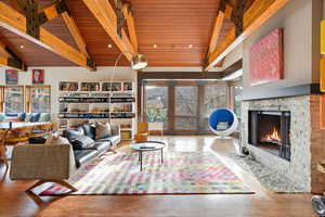 Living room featuring high vaulted ceiling, a stone fireplace, wood finished floors, and a wooden ceiling with exposed beams