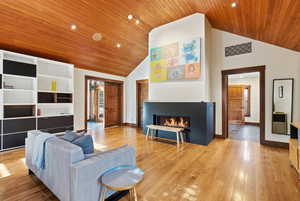 Living room featuring wood ceiling, a glass covered fireplace, high vaulted ceiling, recessed lighting, and light wood-type flooring