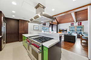 Kitchen featuring high quality appliances, island exhaust hood, lofted ceiling with beams, light countertops, and modern cabinets