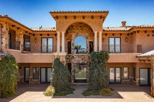 Back of house with stone siding, french doors, stucco siding, a balcony, and a patio