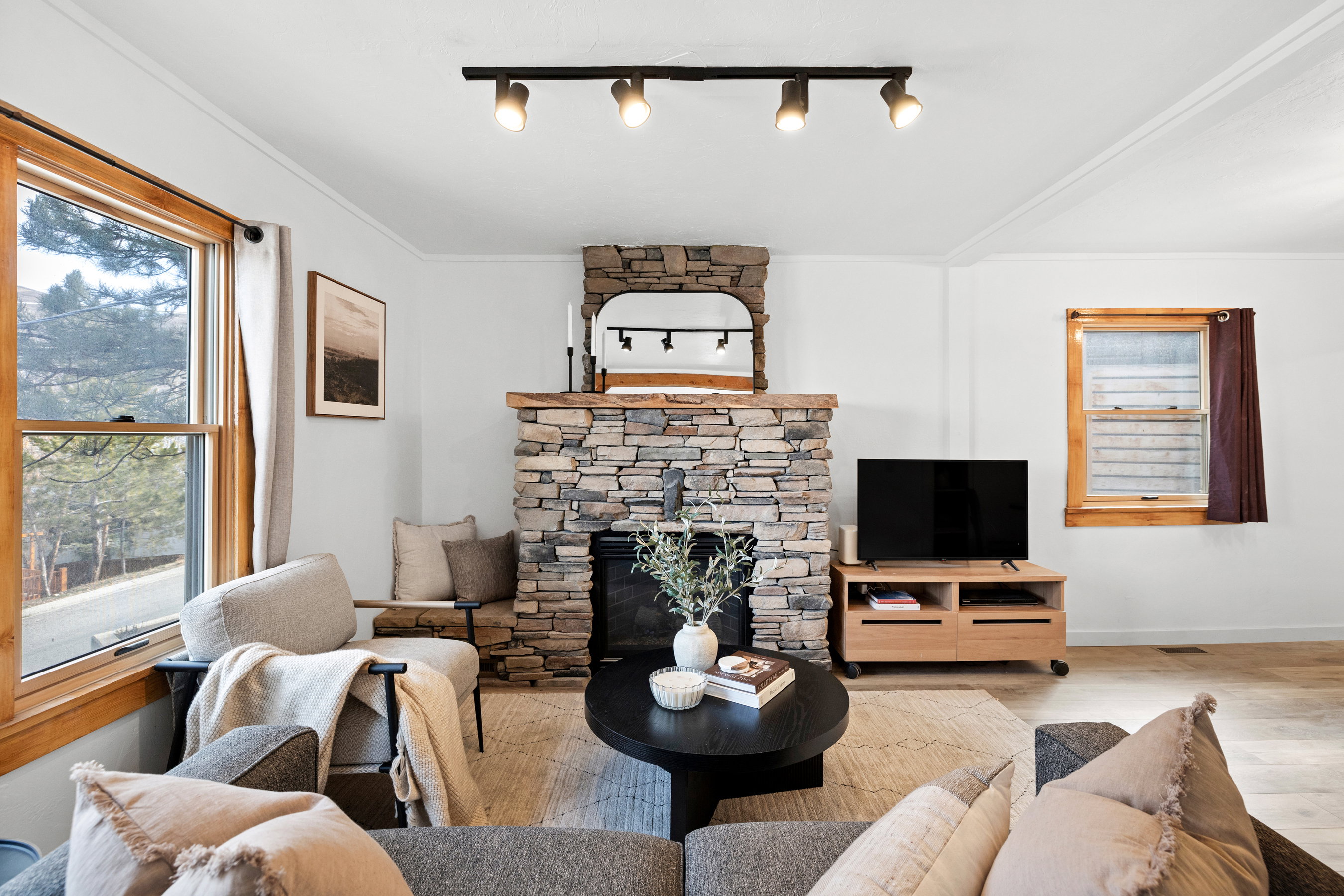 Living room featuring a stone fireplace, wood finished floors, track lighting, and ornamental molding