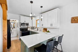 Kitchen featuring white cabinetry, a kitchen breakfast bar, hanging light fixtures, black appliances, and light wood-type flooring