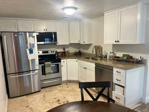 Kitchen featuring appliances with stainless steel finishes, white cabinetry, a textured ceiling, and dark stone countertops