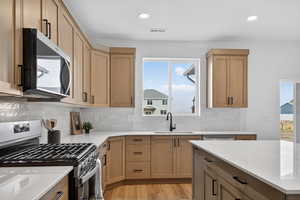 Two tone kitchen featuring stainless steel appliances, two tone cabinetry, light wood-style floors, healthy amount of natural light, and light stone countertops
