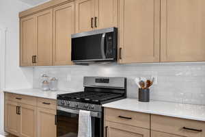 Kitchen with stainless steel appliances, decorative backsplash, light wood finish cabinets, and light stone countertops