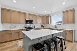Kitchen with stainless steel appliances, a breakfast bar area, light stone countertops, light wood finished floors, and two tone cabinetry