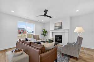 Living area with light wood-type flooring, a ceiling fan, a glass covered fireplace, and recessed lighting