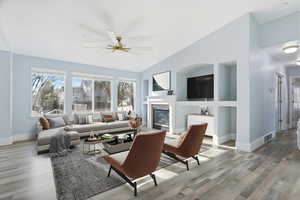 Living room featuring a glass covered fireplace, ceiling fan, light wood finished floors, lofted ceiling, and built in features
