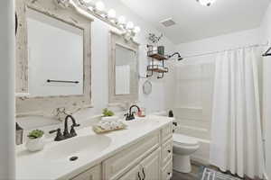 Full bath with double vanity, shower / bath combo, and dark wood finished floors