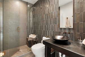 Bathroom with tile walls, a shower stall, vanity, and backsplash
