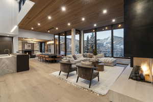 Living area with a lit fireplace, a wall of windows, a mountain view, light wood-style flooring, and wooden ceiling