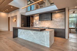 Indoor wet bar featuring modern cabinets, recessed lighting, dark stone countertops, exhaust hood, and light wood-style floors