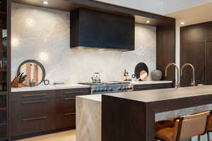 Kitchen with dark wood finish cabinetry, modern cabinets, ventilation hood, light stone counters, and a kitchen bar
