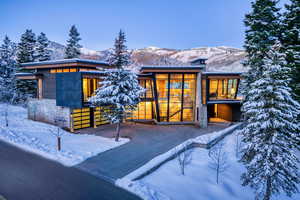 Snow covered back of property featuring a mountain view, a balcony, stone siding, and a chimney