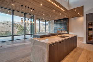 Kitchen featuring modern cabinets, floor to ceiling windows, wood ceiling, hanging light fixtures, and light stone counters