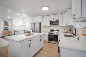 Kitchen with appliances with stainless steel finishes, white cabinetry, light stone countertops, light wood-style flooring, and recessed lighting