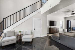 Living room with a ceiling fan, finished concrete floors, recessed lighting, stairway, and a towering ceiling