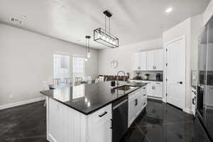 Kitchen with a center island with sink, dishwasher, freestanding refrigerator, hanging light fixtures, and dark stone countertops
