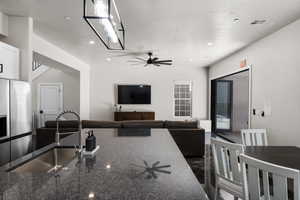 Kitchen featuring dark stone counters, stainless steel fridge with ice dispenser, recessed lighting, ceiling fan, and open floor plan