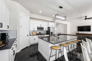 Kitchen featuring open floor plan, a breakfast bar area, a kitchen island with sink, pendant lighting, and dark stone counters