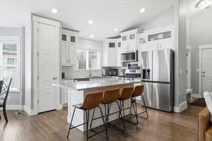 Kitchen with a breakfast bar, a center island, appliances with stainless steel finishes, white cabinets, and lofted ceiling
