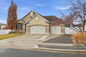 Traditional-style house with stucco siding, stone siding, driveway, a gate, and an attached garage