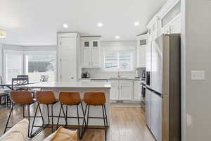 Kitchen featuring appliances with stainless steel finishes, white cabinetry, a breakfast bar, light wood-type flooring, and a center island