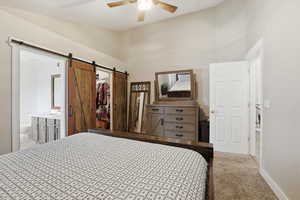 Bedroom featuring carpet, a ceiling fan, a walk in closet, ensuite bath, and a barn door