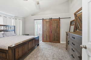 Bedroom featuring lofted ceiling, a barn door, light colored carpet, ceiling fan, and ensuite bath