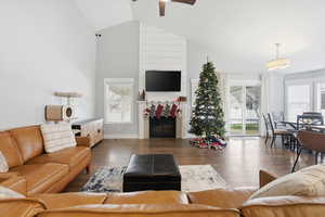 Living room featuring a fireplace, high vaulted ceiling, dark wood-style flooring, and ceiling fan