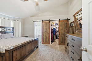 Bedroom with vaulted ceiling, a walk in closet, light colored carpet, and a ceiling fan