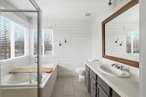 Full bath with a bath, healthy amount of natural light, vanity, wooden walls, and an enclosed shower