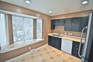 Kitchen featuring freestanding refrigerator, light countertops, dishwasher, dark cabinetry, and recessed lighting
