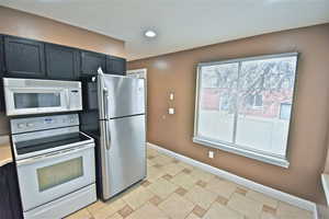 Kitchen with white appliances, dark cabinetry, and recessed lighting