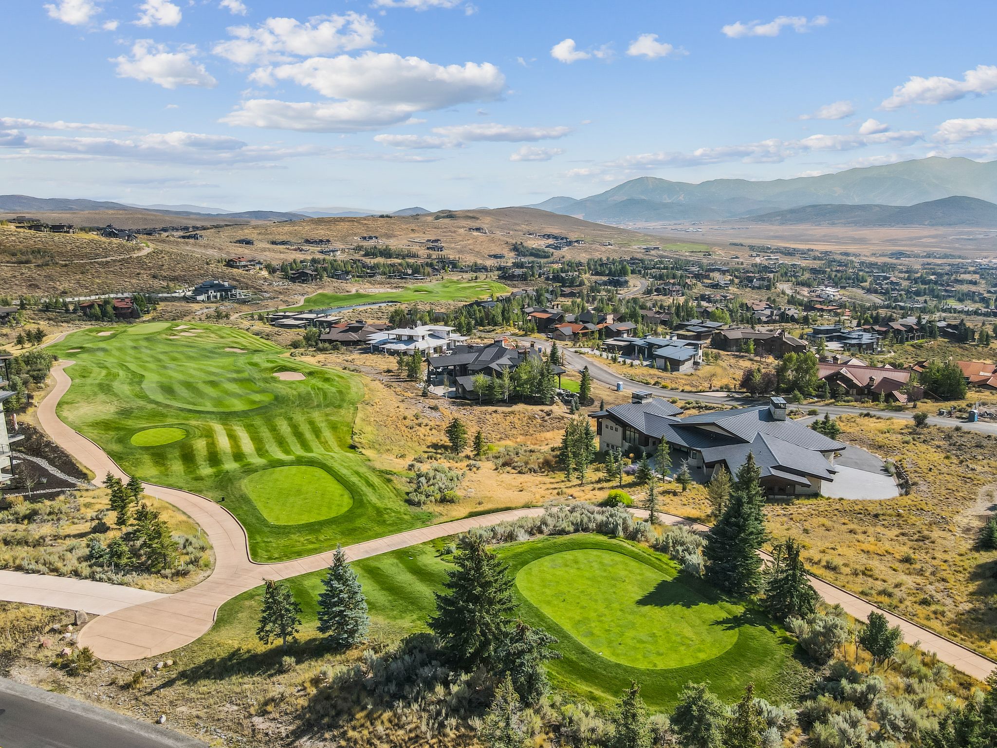 Aerial view of property and surrounding area with a mountain backdrop, a golf course, and nearby suburban area