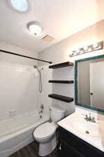 Full bath featuring a textured ceiling, bathing tub / shower combination, vanity, and dark wood-style flooring